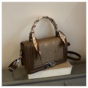 Detail of brown leather handbag featuring metal buckle and silk scarf on handle