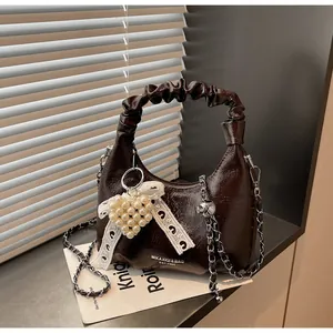 Detailed view of dark brown glossy patent leather bag with pearl heart and chain strap