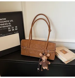 Detail of a brown shoulder bag with a teddy bear charm and silver buckle accent