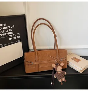 Detail of a brown leather shoulder bag with a cute teddy bear plush charm accessory