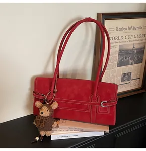 Macro shot of red suede shoulder bag with contrast stitching and teddy bear charm