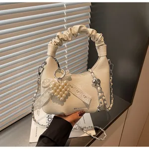 Close-up of cream white pleated PU leather handbag with heart pearl charm and silver chain