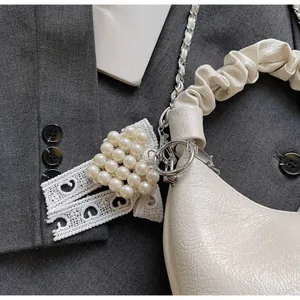 Detail of cream pleated handle bag with silver chain and pearl bow charm accessory