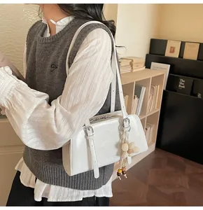 Close-up of white glossy shoulder bag with metal buckle and floral knitted charm