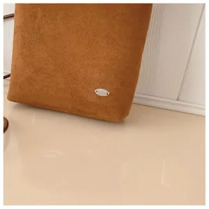 Détail du sac bandoulière en daim marron montrant la texture mate et la plaque en argent