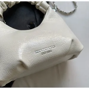 Detail of ruched cream mini handbag with silver metal chain and embossed logo