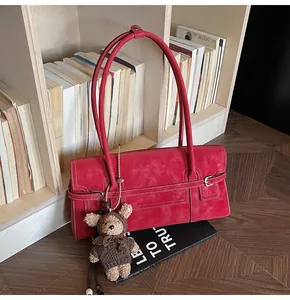Detailed view of red suede shoulder bag with contrast stitching and teddy bear charm