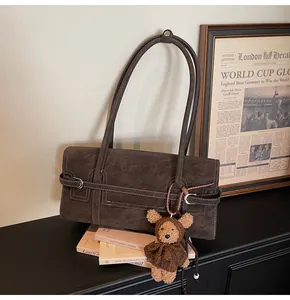 Detail view of vintage brown leather shoulder bag with white stitching and plush bear charm