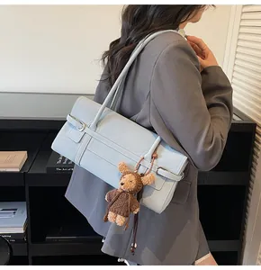 Detail view of a light blue underarm bag with a plush bear charm on a model's shoulder