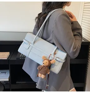 Detail of light blue rectangle shoulder bag with a brown plush bear charm and metal buckles
