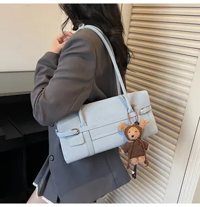 Detail of light blue shoulder bag with leather texture and cute plush bear charm
