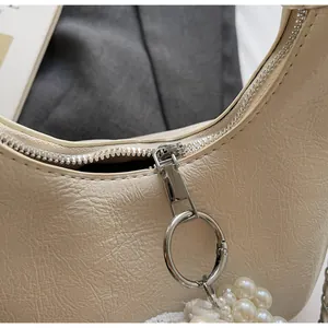 Detail of pleated beige mini handbag with silver ring zipper and pearl chain accessory