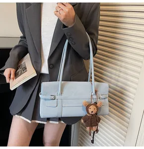 Detail of light blue PU leather shoulder bag with buckle straps and teddy bear charm