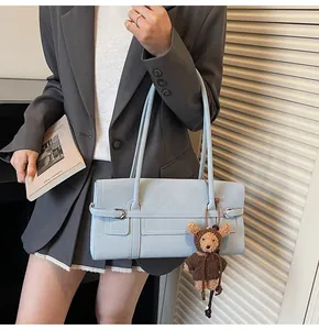 Detail of light blue rectangular shoulder bag with strap buckle and bear charm on model