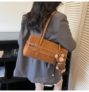 Detail of vintage brown shoulder bag with white contrast stitching and cute teddy bear charm