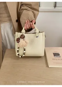 Detail of off-white lychee texture leather tote bag with fashion embossing and puppy charm