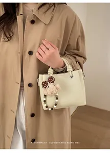 Detail of cream leather tote featuring knot handles and a cute plush bear charm accessory