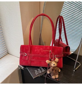 Macro shot of red suede shoulder bag featuring a teddy bear charm and metal buckle