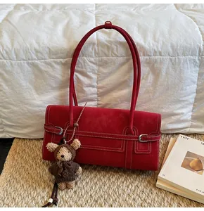 Detail of burgundy suede shoulder bag with white stitching and cute teddy bear charm
