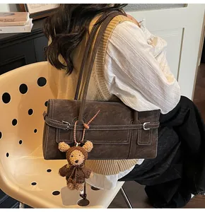 Detail of dark brown vintage shoulder bag with contrast stitching and bear charm