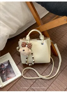 Detail of creamy white pebble grain tote bag with plush bear charm and beaded chain