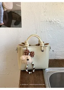 Close-up of cream textured leather handbag with a cute plush bear charm on wooden surface