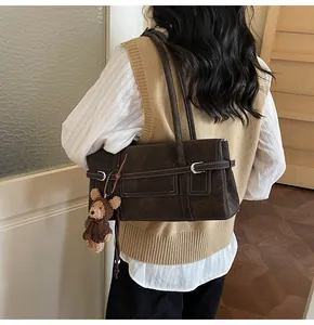 Detail of vintage brown suede shoulder bag with contrast stitching and plush bear charm