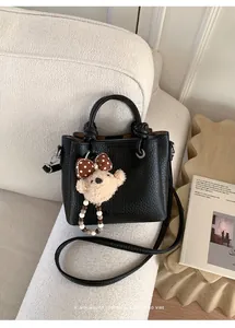 Close-up of black litchi textured tote bag with a cute bear charm on a sofa