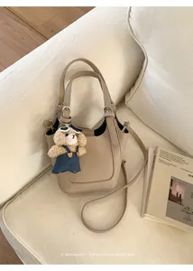 Detail van beige lederen emmertas met een schattige berenhanger op de bank getoond