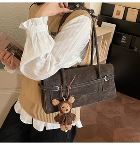 Detail of dark brown suede shoulder bag featuring contrast stitching and bear charm