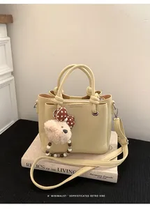 Detail of light yellow leather bucket bag with cute plush bear charm and bow decoration