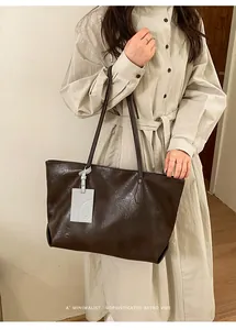 Detail of dark brown leather tote bag with a decorative tag held by a model