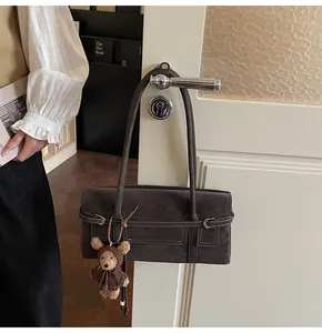 Detail of vintage matte leather shoulder bag with buckle strap and cute teddy bear charm