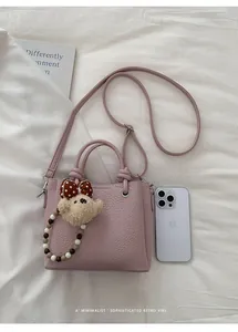 Detail of pink pebbled leather bucket bag with cute bear charm and fashion logo