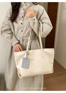 Detail of minimalist cream tote bag with a grey cat embossed decorative pendant