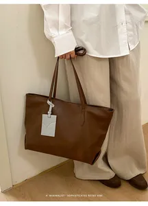 Minimalist brown leather tote bag with tag detail shown held by model in indoor setting