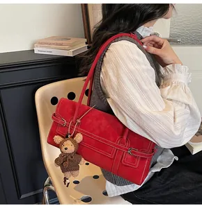 Detail of red suede shoulder bag with metal buckles and a cute plush bear charm