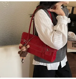 Detail view of red vintage shoulder bag with contrast stitching and teddy bear charm