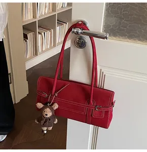 Detail of red leather shoulder bag with white contrast stitching and a small bear charm
