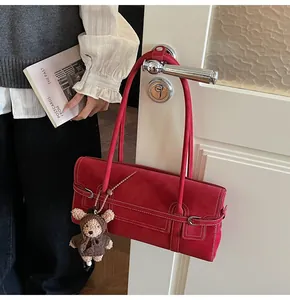 Detail of dark red faux suede shoulder bag with white stitching and plush bear charm