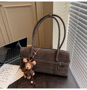 Detail of dark brown suede shoulder bag with white stitching and bear plush charm