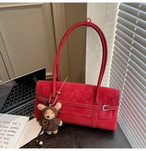 Detail of red suede shoulder bag featuring a silver buckle and cute plush bear charm