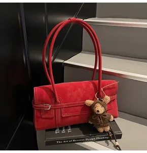 Detail of red suede shoulder bag with silver buckle and decorative plush bear pendant