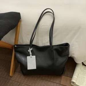 Minimalist black faux leather tote bag with a white animal charm in a cozy indoor scene