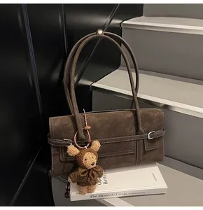 Detail view of dark brown faux suede shoulder bag with buckle strap and bear charm
