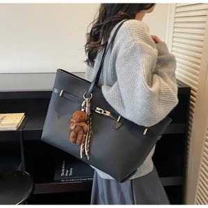 Detail of black pebbled leather tote bag with a plush bear charm on a chic shoulder strap
