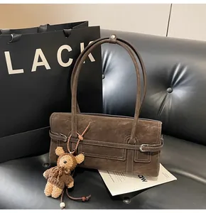 Detail of dark brown suede baguette bag featuring thin shoulder strap and bear charm decoration