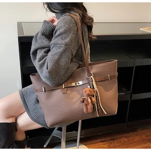 Detail view of deep brown suede tote bag with decorative buckle and bear charm