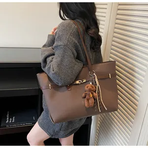 Detail of dark brown tote bag with metal twist lock, plush bear charm and tassel