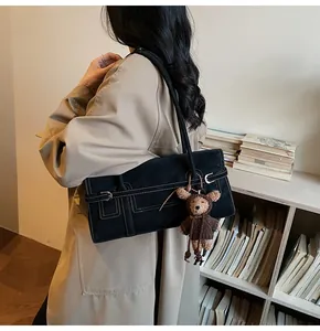 Detail of vintage black suede shoulder bag with bear charm on a khaki trench coat